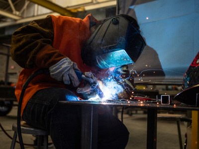 A person welding a piece of metal while wearing protective gear and a mask.