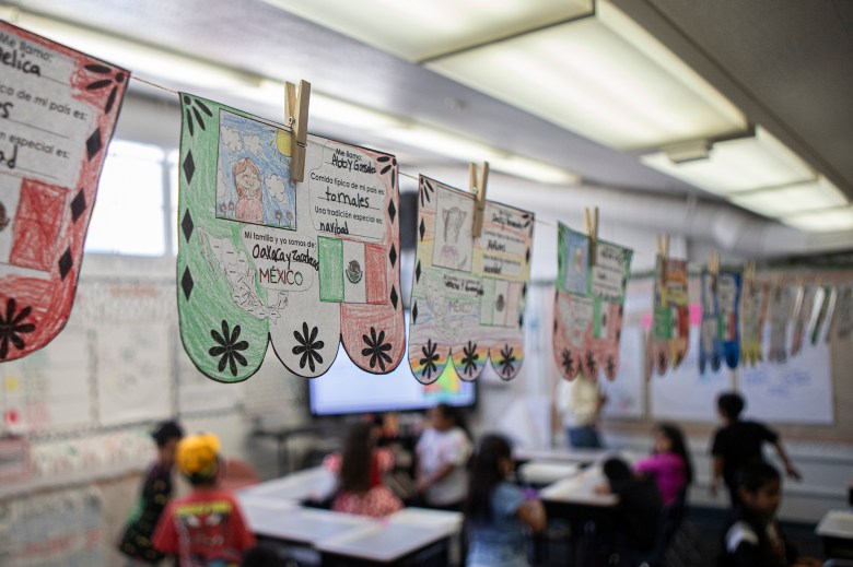 A cord runs along the length of a classroom. Pieces of paper are suspended by clothes pins from the cord. The papers are children's drawings.